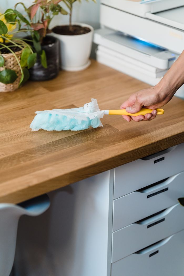services-img A hand using a feather duster to clean a wooden desk, surrounded by plants and office items.